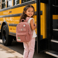 Girl boarding the school bus with a pink small backpack knitted with Amelia