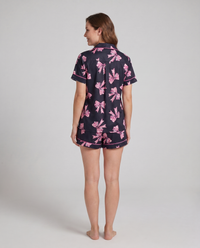 Black button-up pajama shirt detail — blush ribbon-bow print on midnight black stretch fabric
