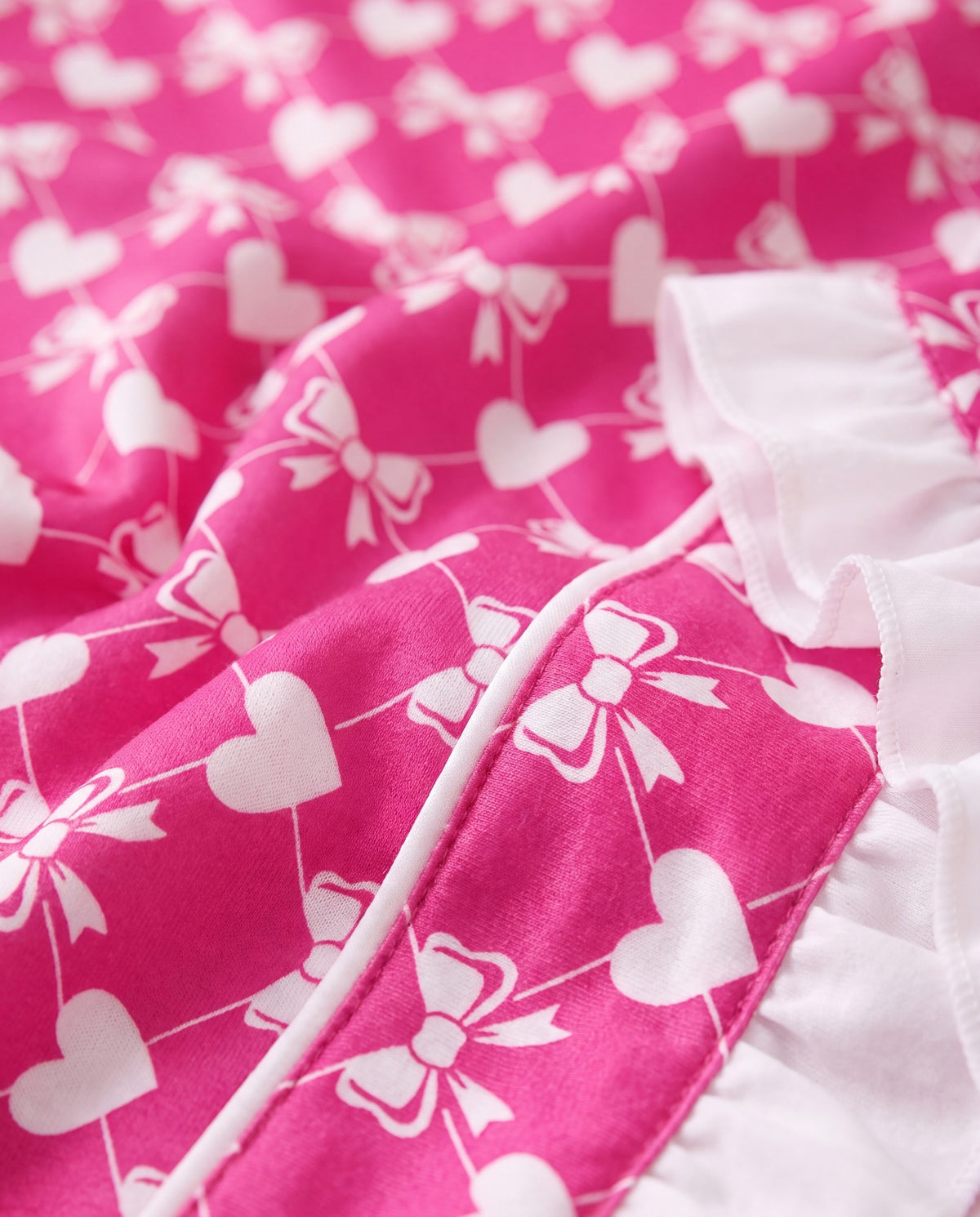 Close-up of the white heart and ribbon bow print on hot pink fabric