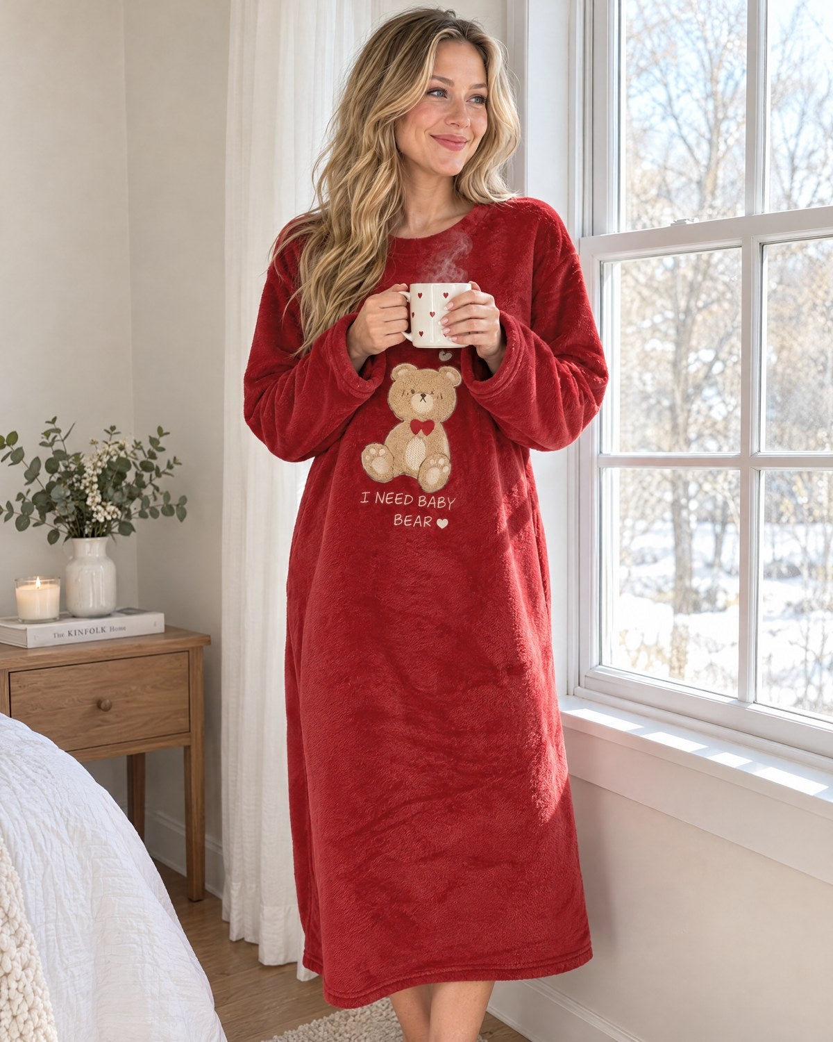 Woman holding a steaming mug by a snowy window in the Bear Hug Fleece Nightgown
