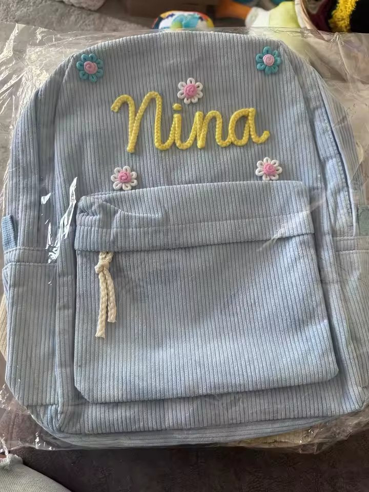 Light blue backpack with Nina in yellow wool and flower charms