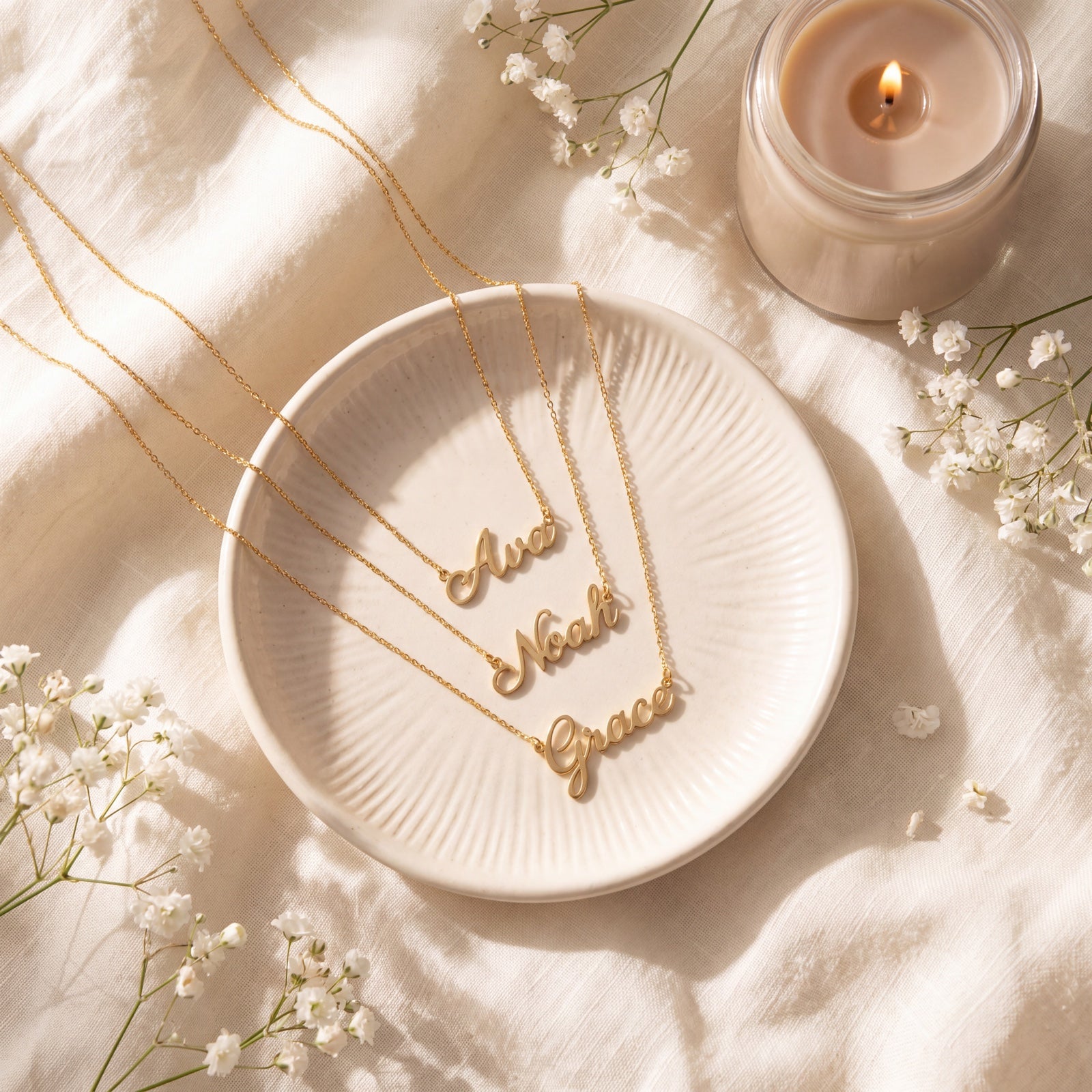 Three gold personalized name necklaces reading Ava, Noah and Grace on a cream jewelry dish