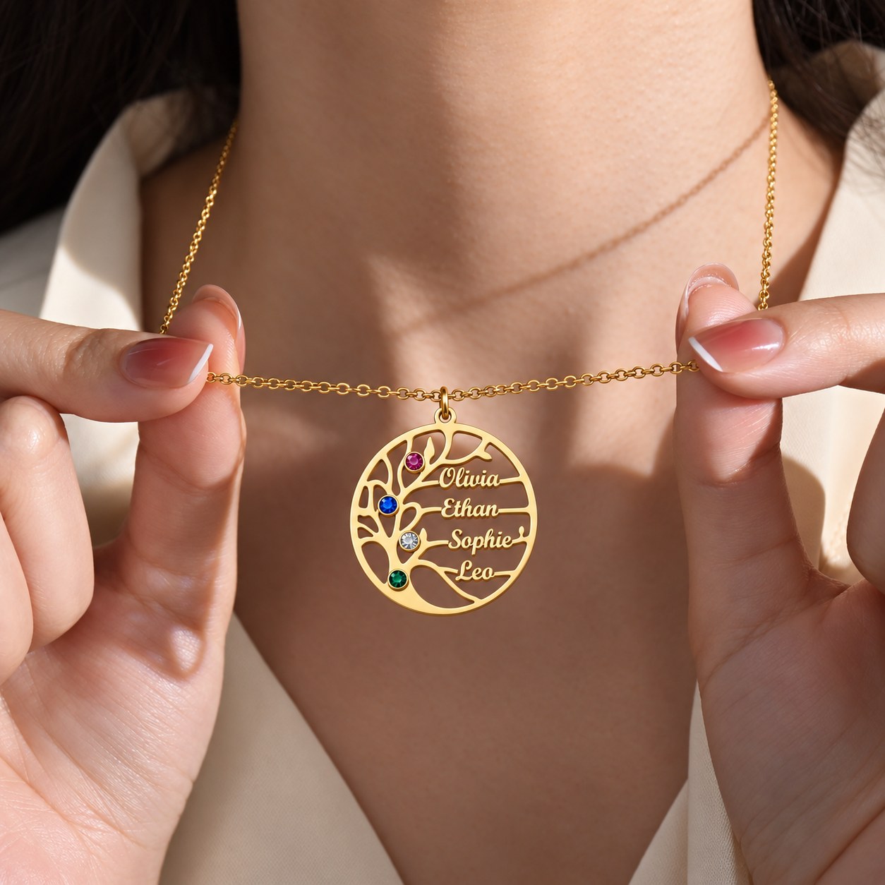 Hands holding the gold family tree pendant engraved Olivia, Ethan, Sophie and Leo with four birthstones